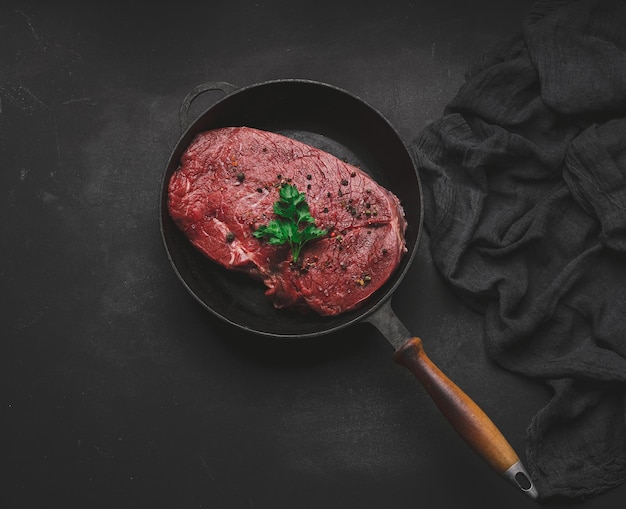 Raw beef tenderloin lies in a metal round frying pan on a black tab