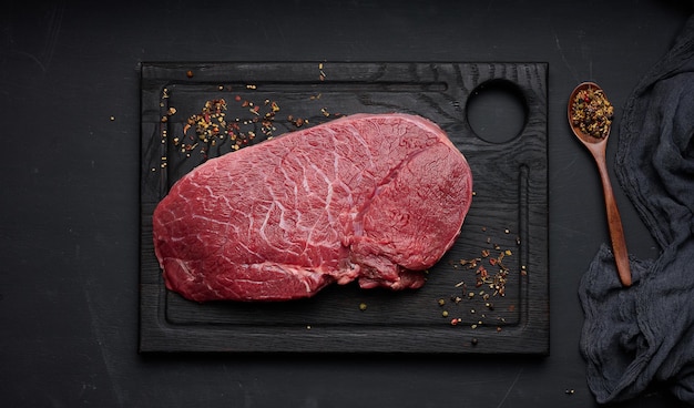 Raw beef tenderloin lies on a wooden cutting board on a black table top view