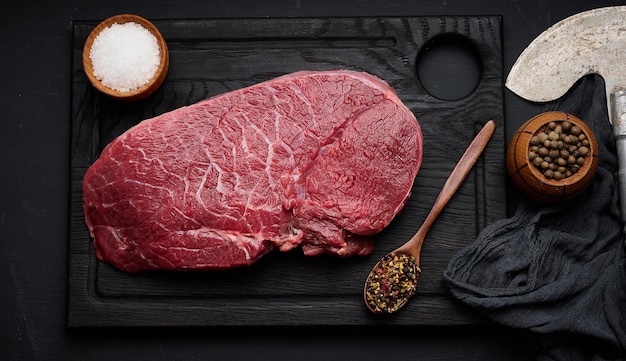 Raw beef tenderloin lies on a wooden cutting board on a black table top view