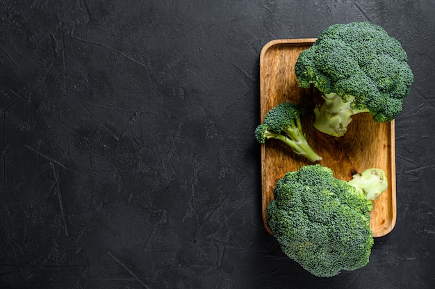 Raw broccoli in a wooden bowl. Black background. Top view. Space for text.