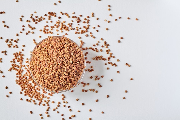 Raw buckwheat groats in a transparent glass plate on white background