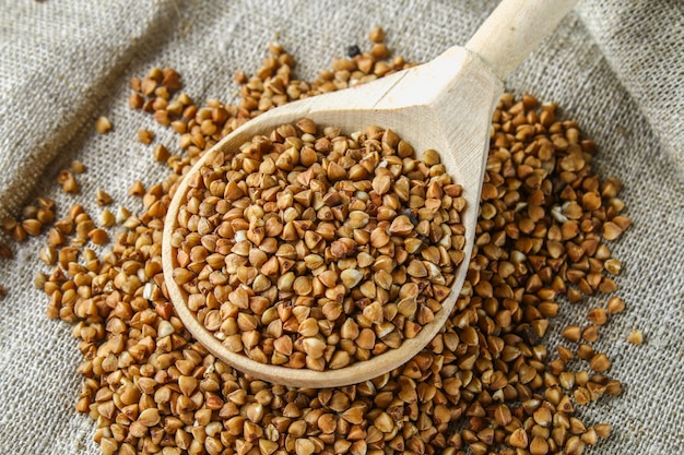 Raw buckwheat in a spoon on sackcloth on a wooden background. Healthy diet food