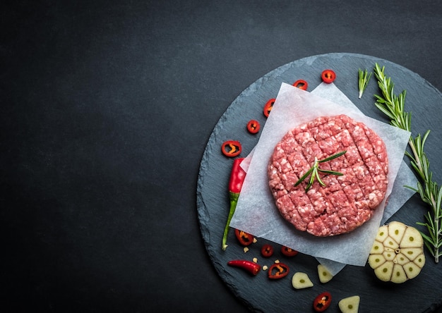 Raw burger beef patty with rosemary and garlic on dark cooking background