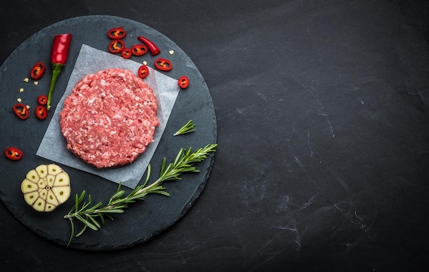 Raw burger cutlet from beef meat with garlic and rosemary on black background with copy space top vi