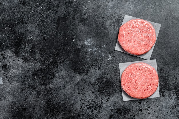 Raw Burger patties, ground beef meat on black. Top view. Copy space