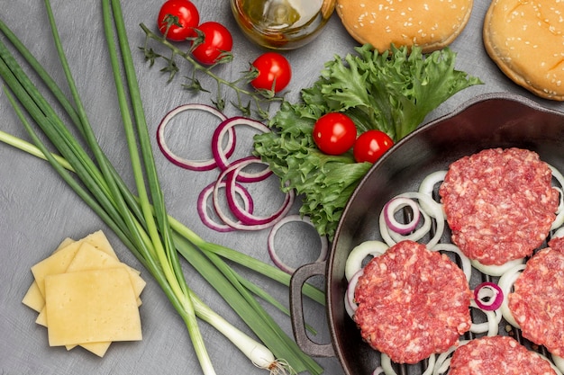 Raw burgers with onions in a frying pan