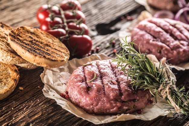 Raw burgers on wooden table with onion tomatoes herbs and spices.