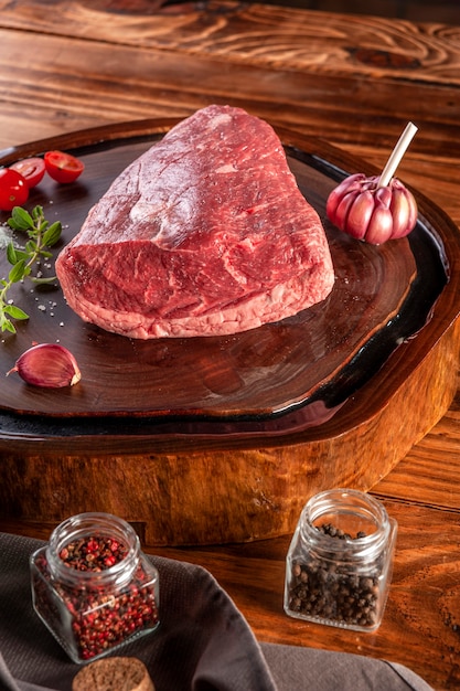 Raw cap rump beef (brazilian picanha) on a wood resined cutting board with spices. Wooden table.