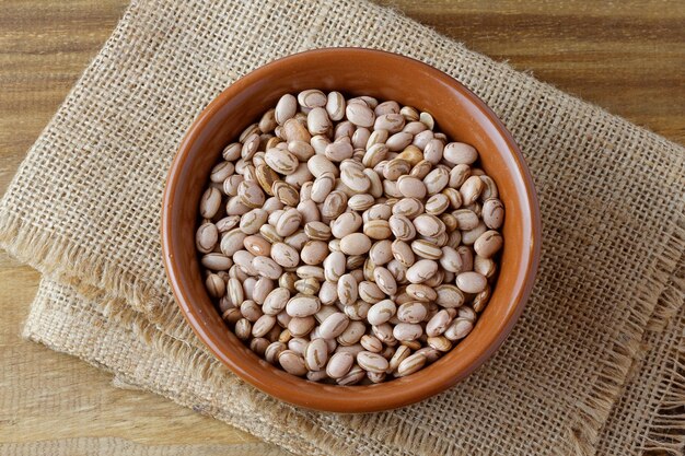 Raw carioca beans in bowl over rustic wooden table Product name in Brazilian Portuguese Top view