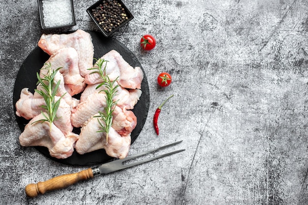 Raw chicken on a black plate with spices and herbs.