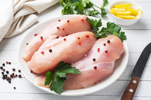 Raw chicken breast fillet on a plate, white wooden background.