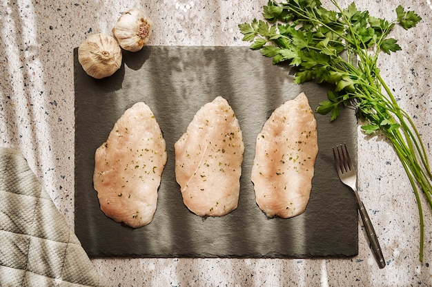 Raw chicken breast fillets on a slate on a granite table with parsley