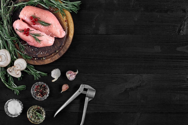 Raw chicken breast fillets on wooden cutting board with herbs spices and mushrooms on a black wooden background Top view with copy space Still life Flat lay