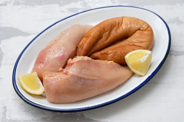 Raw chicken breast with smoked sausage and lemon on dish