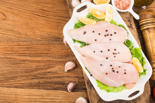 Photo raw chicken breasts and spices on wooden cutting board