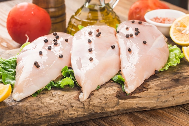 Photo raw chicken breasts and spices on wooden cutting board,