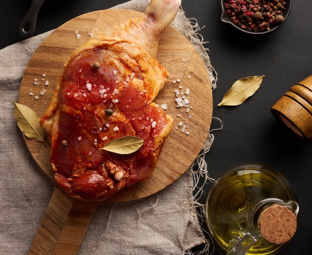 Raw chicken drumsticks seasoned on a wooden board accompanied by salt and peppercorns