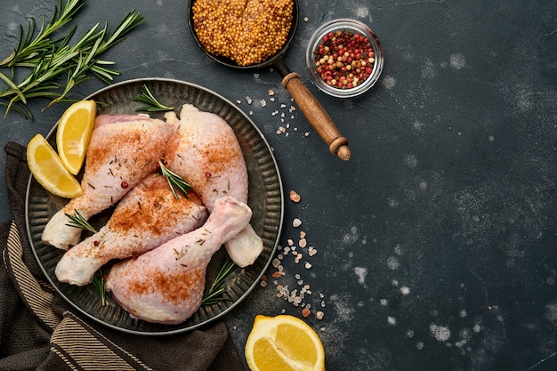 Raw chicken drumsticks with ingredients for cooking on a black stone surface. Top view.