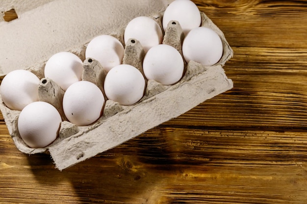 Raw chicken eggs in cardboard egg box on wooden table Top view