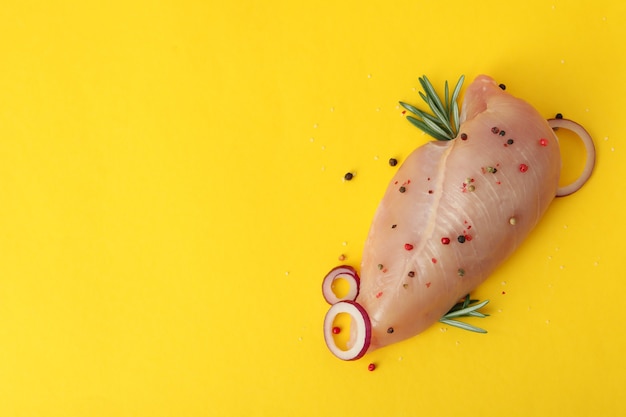 Raw chicken fillet with spices on yellow background