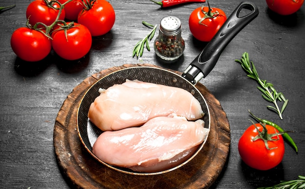 Raw chicken fillet with tomatoes and herbs on the black chalkboard.