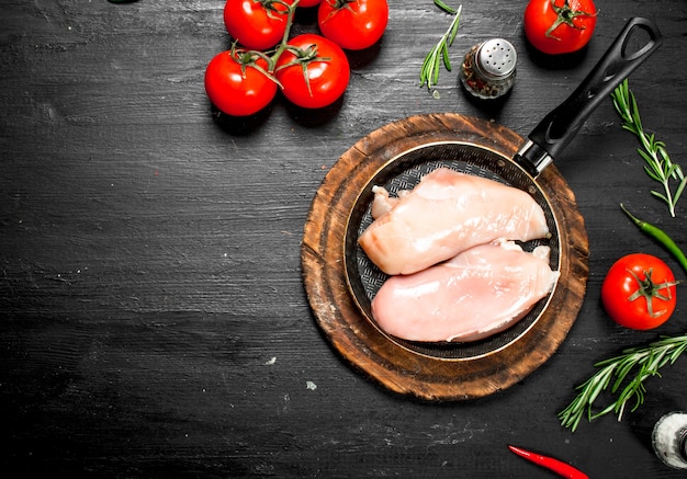 Raw chicken fillet with tomatoes and herbs on the black chalkboard.