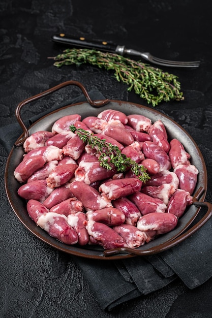 Raw chicken hearts in a steel tray with thyme Black background Top view