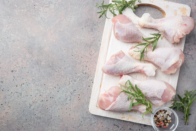 Raw chicken legs with herbs and spices on cutting board.