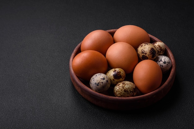 Raw chicken and quail eggs in a brown ceramic bowl on a dark concrete background