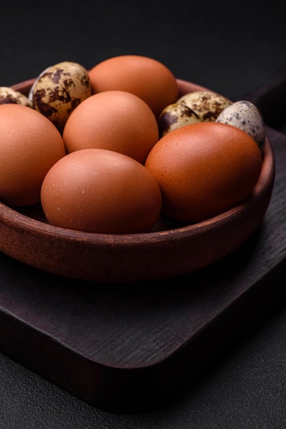 Raw chicken and quail eggs in a brown ceramic bowl on a dark concrete background