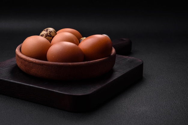 Raw chicken and quail eggs in a brown ceramic bowl on a dark concrete background