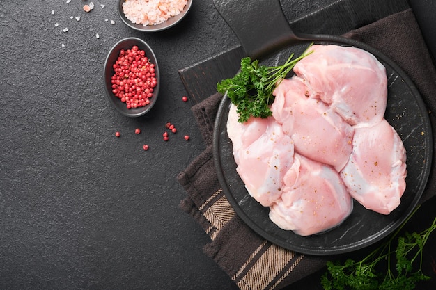 Raw chicken thigh fillet without skin with herbs and spices on black background Farm poultry meat Top view with copy space Mock up