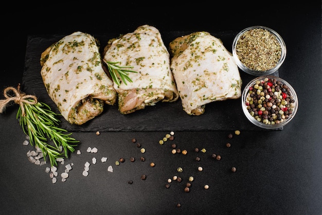 Raw chicken thighs marinated in herbal sauce on a dark background with fresh rosemary spices