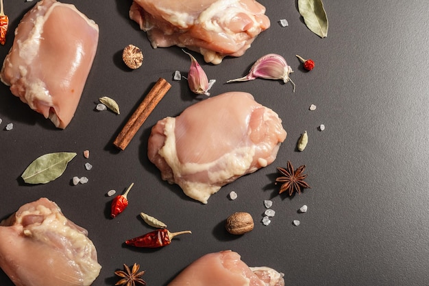 Raw chicken thighs without bones or skin. A useful ingredient for preparing healthy food, spices, garlic. Black stone background, trendy hard light, dark shadow, top view