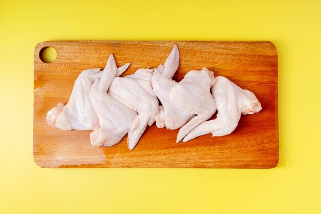 Raw chicken wings on cutting board isolated on yellow background Top view