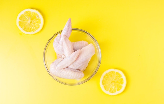 Raw chicken wings in glass bowl isolated on yellow background Top view Copy space