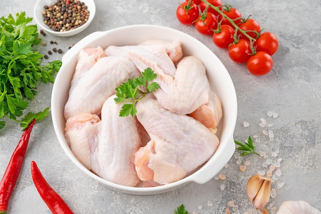 Raw chicken wings in a white dish with fresh herbs spices for cooking Top view copy space