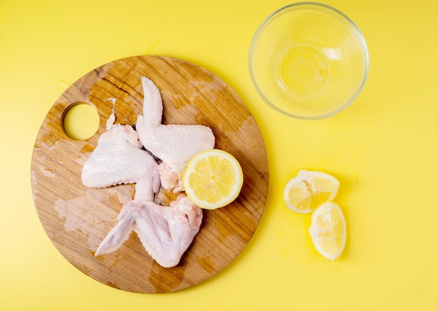 Raw chicken wings with lemon slices on cutting board isolated on yellow background Top view