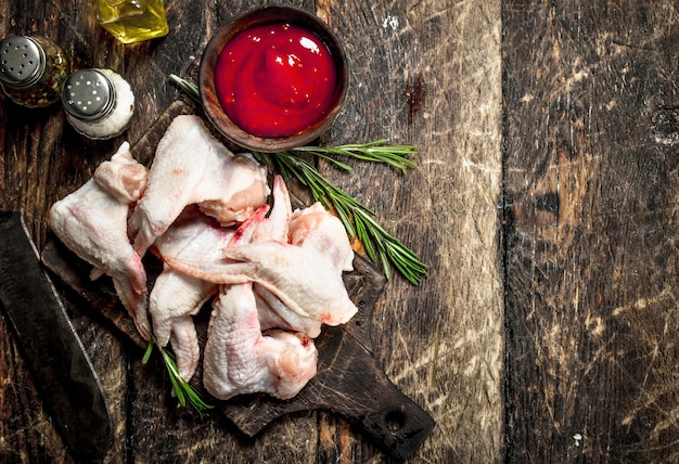 Raw chicken wings with tomato sauce and herbs. On a wooden table.