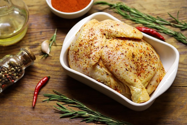 Raw chicken with spices, paprika and rosemary in a ceramic baking dish on a wooden cutting board