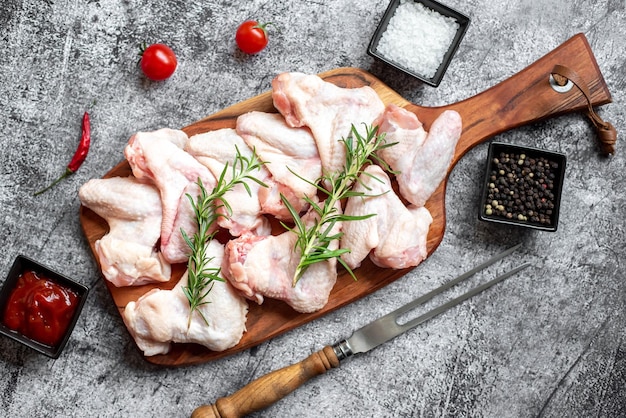 Raw chicken on a wooden board with salt and pepper on a gray background.