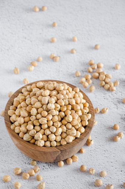 Photo raw chickpeas on a wooden bowl on a light surface chickpeas is nutritious food. healthy and vegetarian food. vertical orientation, copy space.