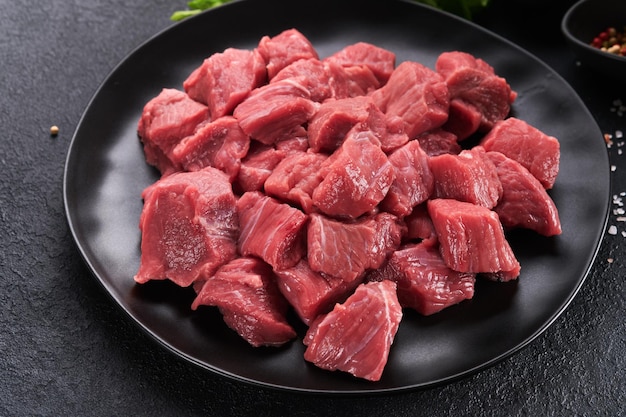 Raw chopped beef meat Raw organic meat beef or lamb spices herbs on black plate on dark grey concrete background Goulash Raw uncooked meat Meat with blood Top view with copy space