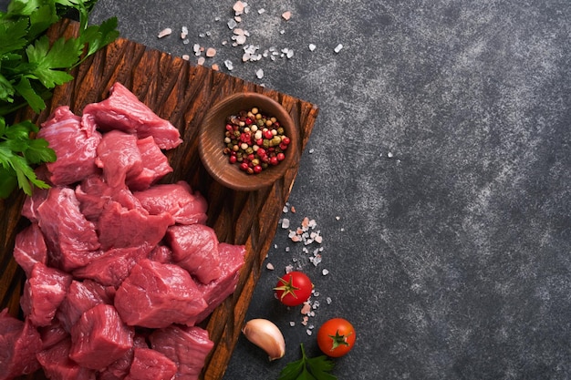 Raw chopped beef meat Raw organic meat beef or lamb spices herbs on old wooden board on dark grey concrete background Goulash Raw uncooked meat Meat with blood Top view with copy space