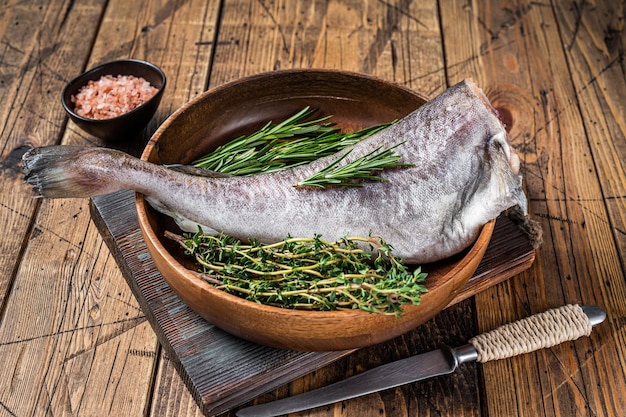 Raw cod or codfish fish in wooden plate with herbs. Wooden background. Top view.