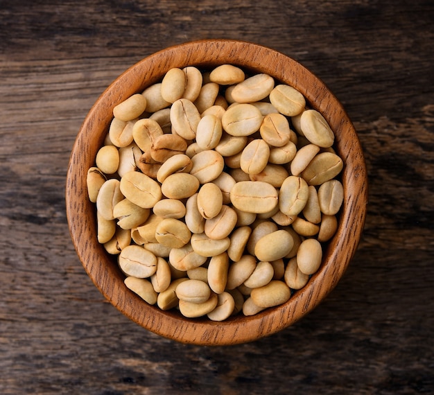 Raw coffee beans in wood bowl on wooden table