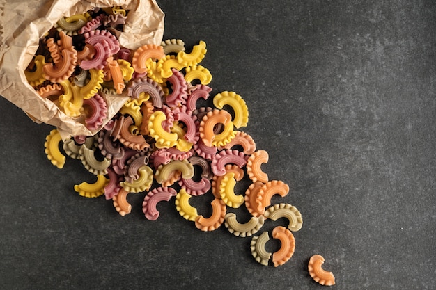 Raw colored pasta scattered on black stone background