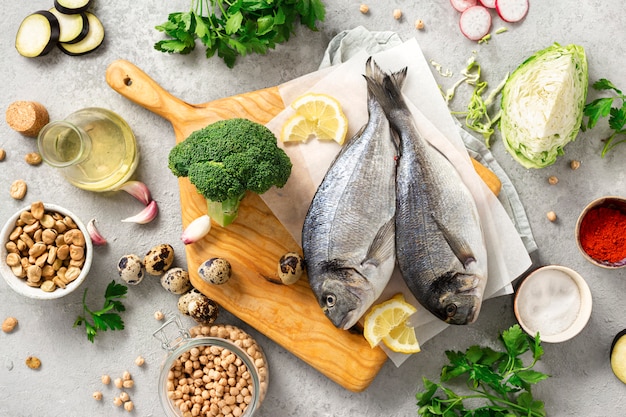 Raw cooking ingredients for tasty and healthy food. Fresh fish, vegetables, herbs and legumes on gray background top view