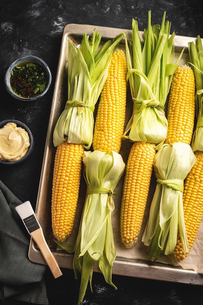 Raw corn on the cob on a baking sheet, top view