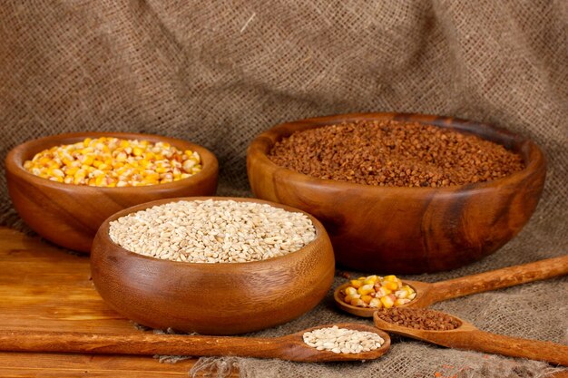 Raw cornbuckwheat and wheat in wooden bowls on table on sackcloth background